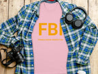 A flat lay photo features a Garment Graphics T-shirt with FBI Female Boob Inspector in yellow. The design is surrounded by a blue plaid shirt, headphones, a camera, and a cup on a wooden surface, highlighting the humorous style.