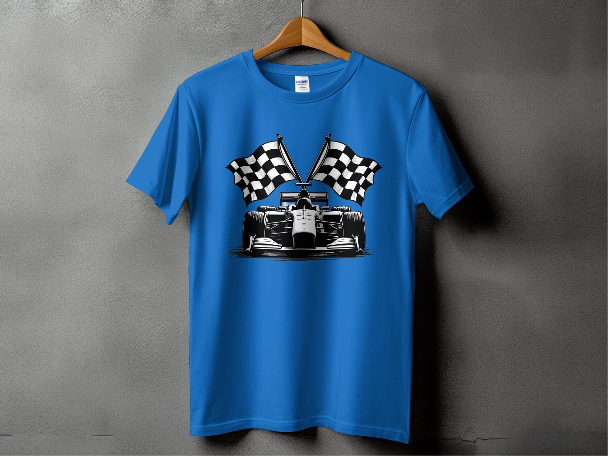 A Garment Graphics blue graphic T-shirt with a motorsport design featuring a racing car and crossed checkered flags hangs on a wooden hanger against a plain, textured gray wall.