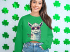 A woman poses in front of a shamrock-covered wall, wearing Garment Graphics green unisex No Prob-Llama sweatshirt featuring a sunglass-wearing llama, styled with denim shorts. She smiles brightly at the camera.