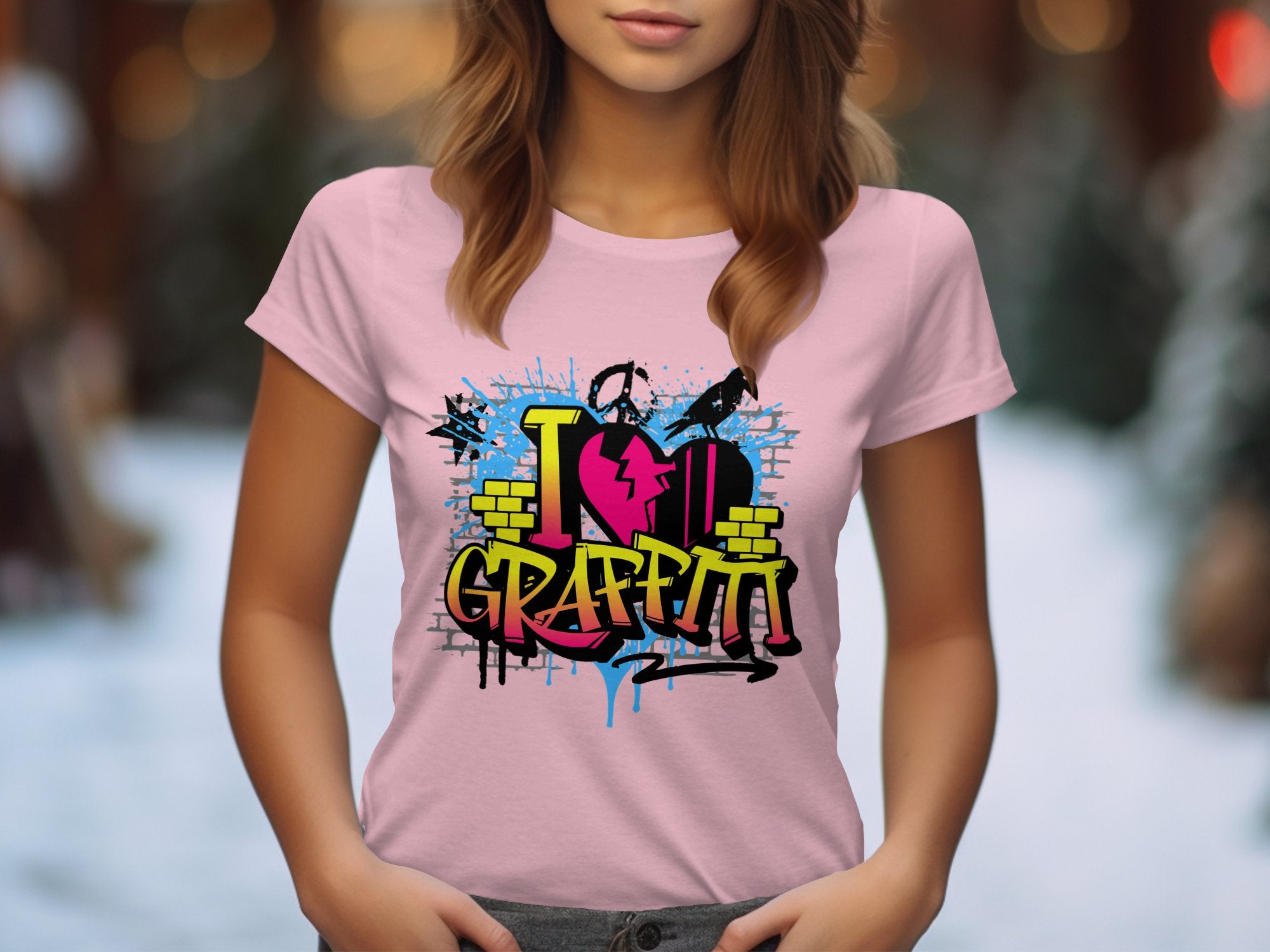 A person wears a Garment Graphics pink T-shirt with I Love Graffiti in vibrant text, featuring paint splatters, spray painter silhouettes, and a heart design—ideal for urban design lovers. The background is softly lit and blurred.