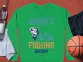 The Garment Graphics green sweatshirt, featuring Daddys Fishing Buddy in blue and orange with a fish graphic, is ideal for outdoor enthusiasts. Pair it with a water bottle, gray towel, black shorts, and basketball on an orange surface for the complete look.