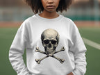 A person with curly hair and an edgy style stands outdoors wearing a Garment Graphics white unisex sweatshirt featuring a large skull and crossbones design, offering a relaxed fit. The out-of-focus field creates an atmospheric backdrop as they gaze ahead.