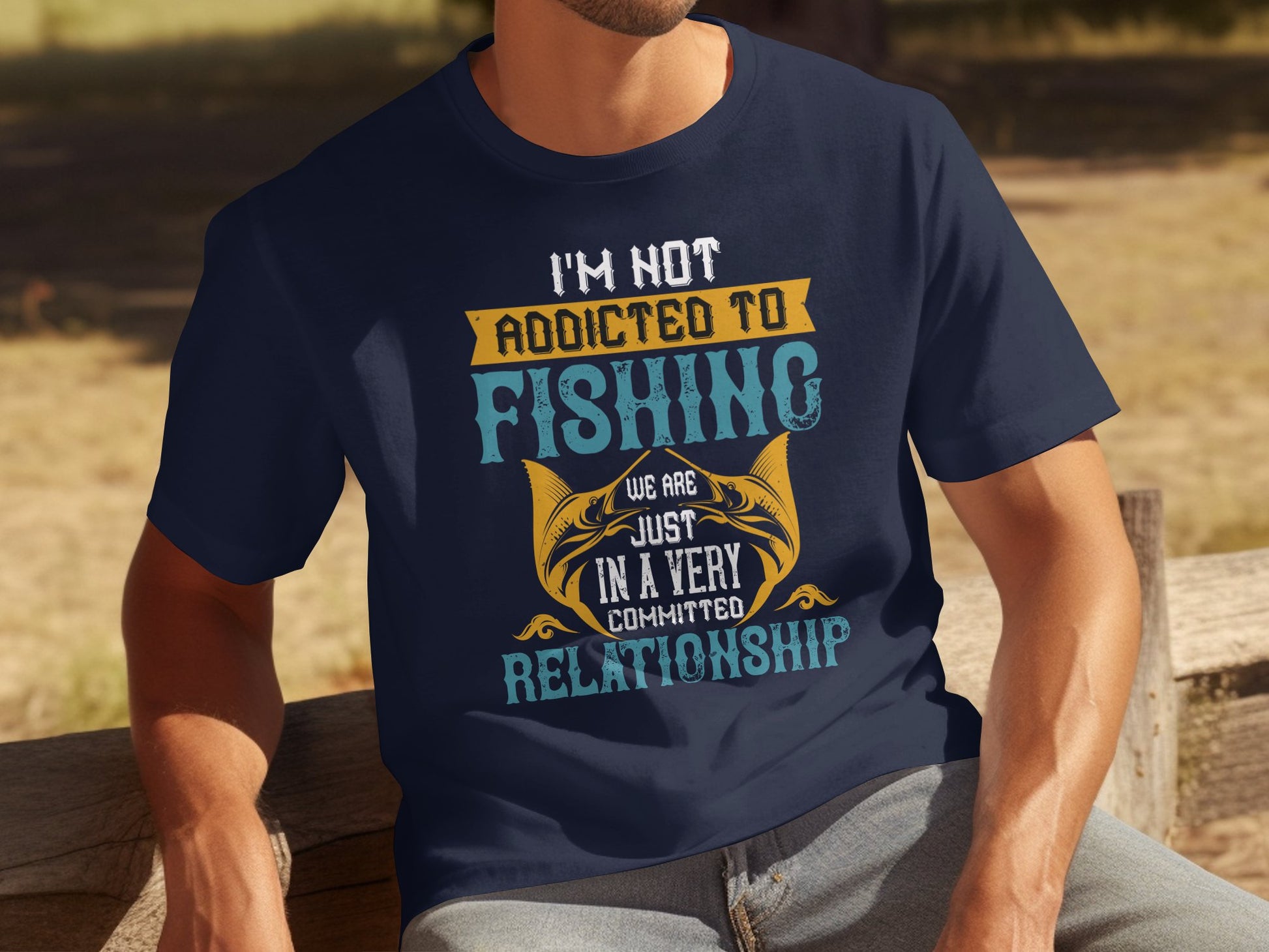 A man sits on a wooden bench wearing a Garment Graphics T-shirt, featuring the fun text: Im not addicted to fishing; we are just in a very committed relationship in various fonts and colors. The blurred outdoor backdrop suits dedicated anglers perfectly.