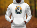 A person dons Garment Graphics Fierce Owl Illustration Hoodie, made from medium-heavy fabric, featuring a vivid owl on an orange circle. The backdrop is a blurred autumn forest with brown leaves and tall trees, enhancing the hoodies distinctive appeal.