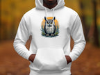 A person dons Garment Graphics Fierce Owl Illustration Hoodie, made from medium-heavy fabric, featuring a vivid owl on an orange circle. The backdrop is a blurred autumn forest with brown leaves and tall trees, enhancing the hoodies distinctive appeal.
