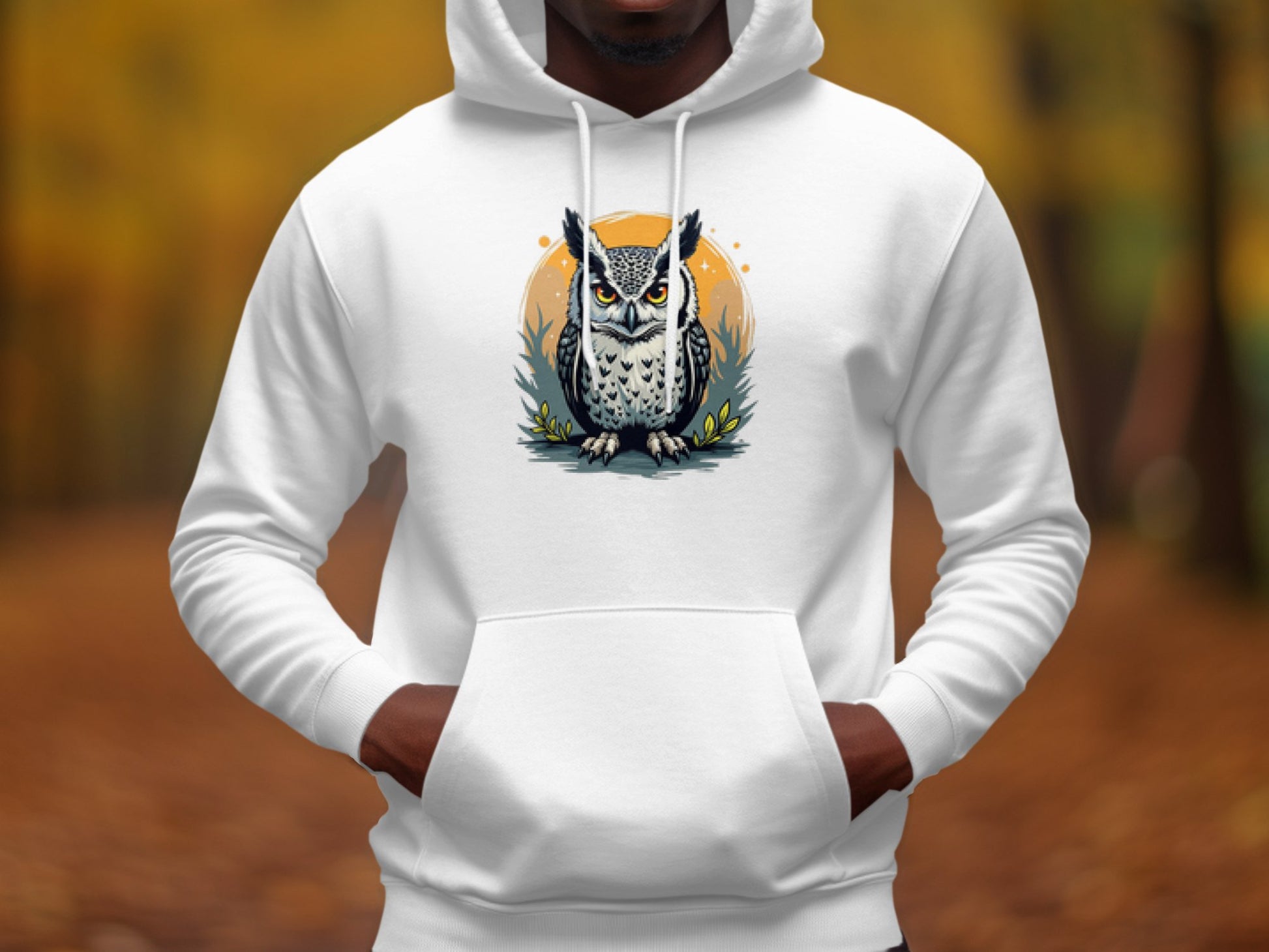 A person dons Garment Graphics Fierce Owl Illustration Hoodie, made from medium-heavy fabric, featuring a vivid owl on an orange circle. The backdrop is a blurred autumn forest with brown leaves and tall trees, enhancing the hoodies distinctive appeal.