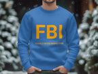 A person is wearing a blue Garment Graphics sweatshirt featuring FBI in bold yellow letters and the playful phrase FEMALE BOOB INSPECTOR. This unisex design suits anyone. Snow-covered trees are visible in the blurred background, enhancing the lighthearted scene.