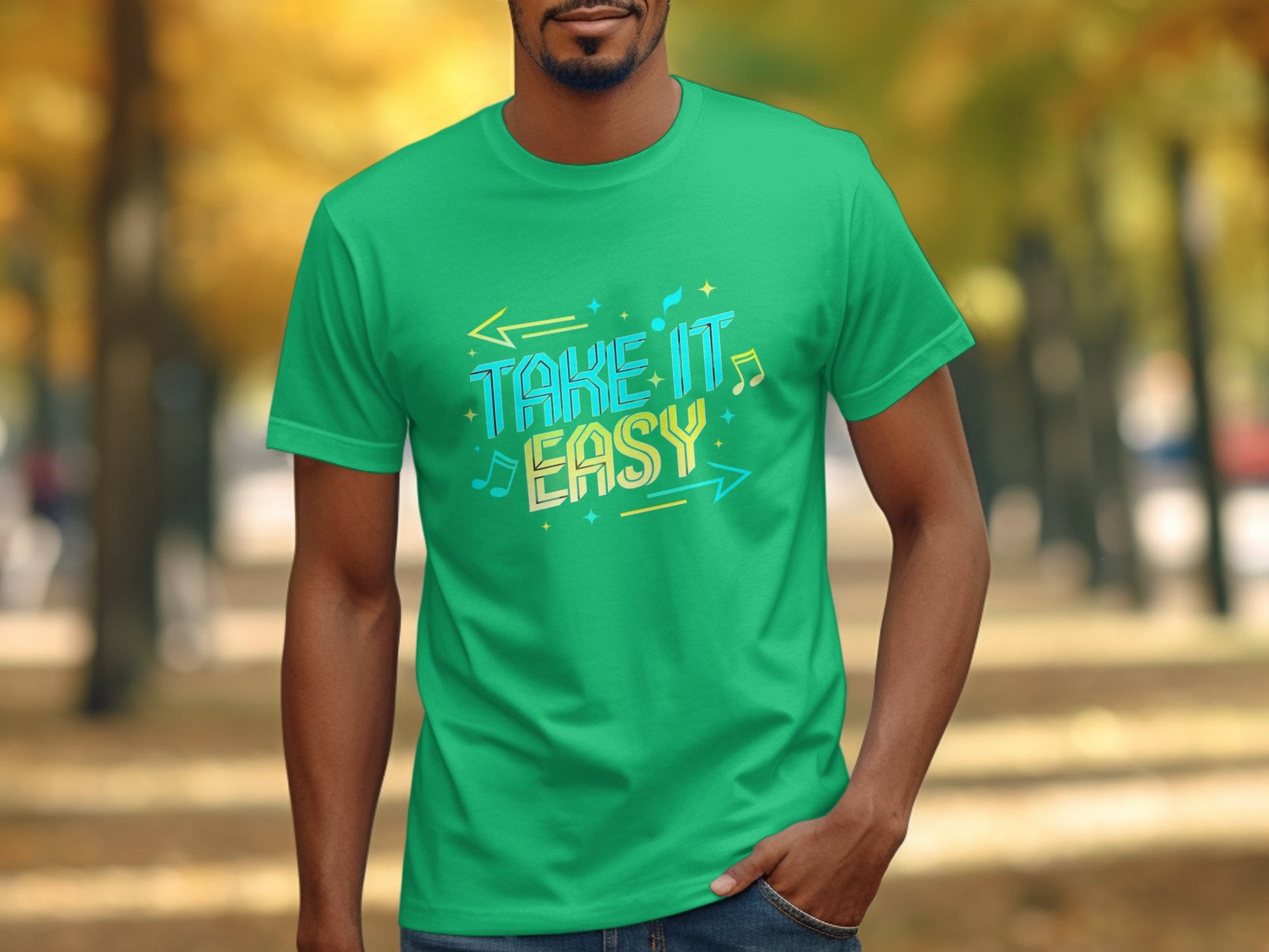 A person in a Garment Graphics green t-shirt with vibrant designs and the colorful phrase Take It Easy stands outdoors, with blurred autumn trees in the background swaying gently like dancers to invisible music.