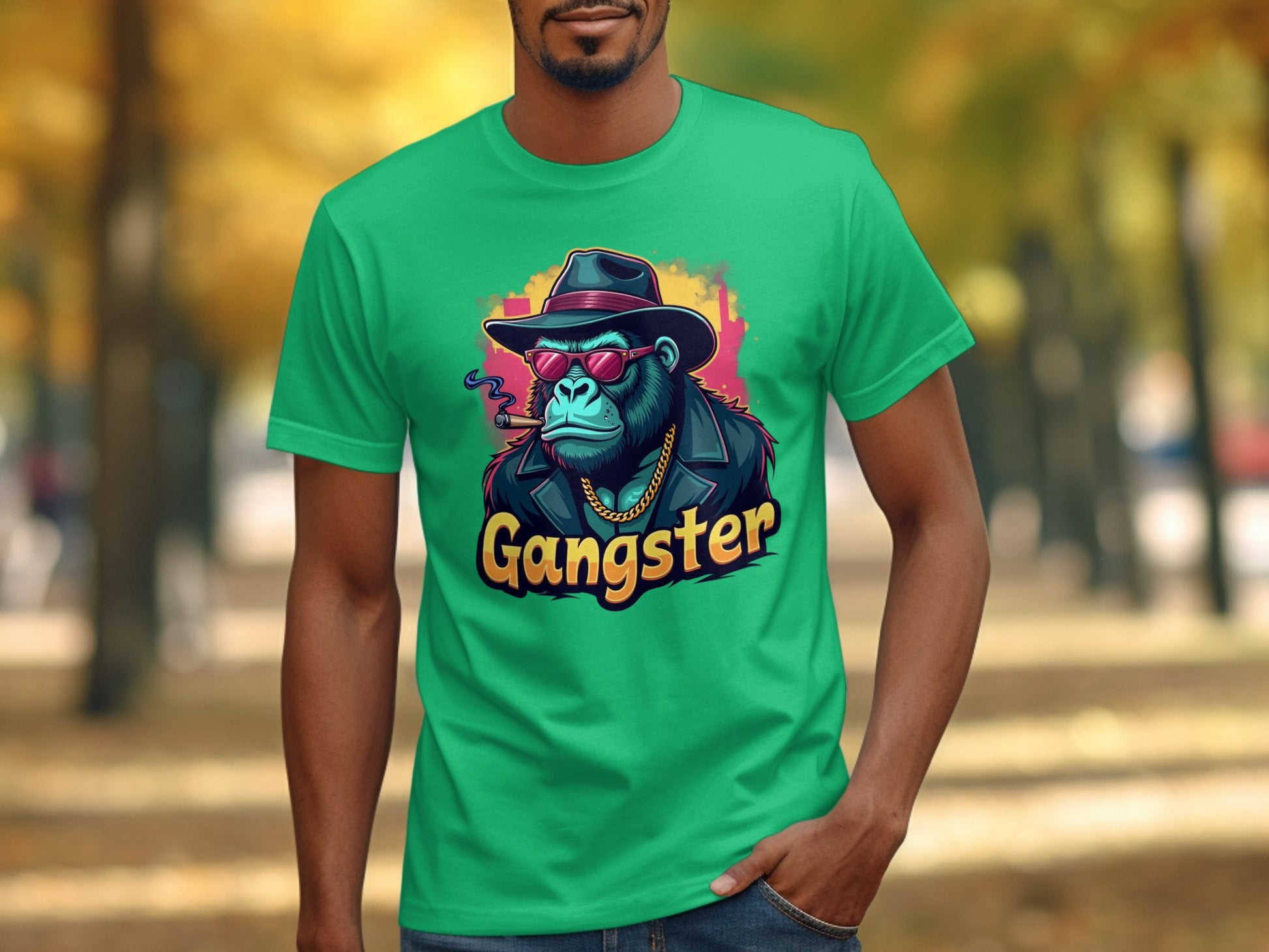 Someone is donning a classic fit green t-shirt from Garment Graphics, featuring a chimpanzee with a hat, sunglasses, and necklace labeled Gangster. This urban style complements the tree-lined path in the background with scattered leaves.