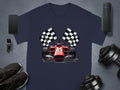 Garment Graphics presents a blue t-shirt showcasing a race car and crossed checkered flags, ideal for motorsport fans. Its set against a gray backdrop with a smartphone, smartwatch, sneakers, wireless speaker, and dumbbell weights.