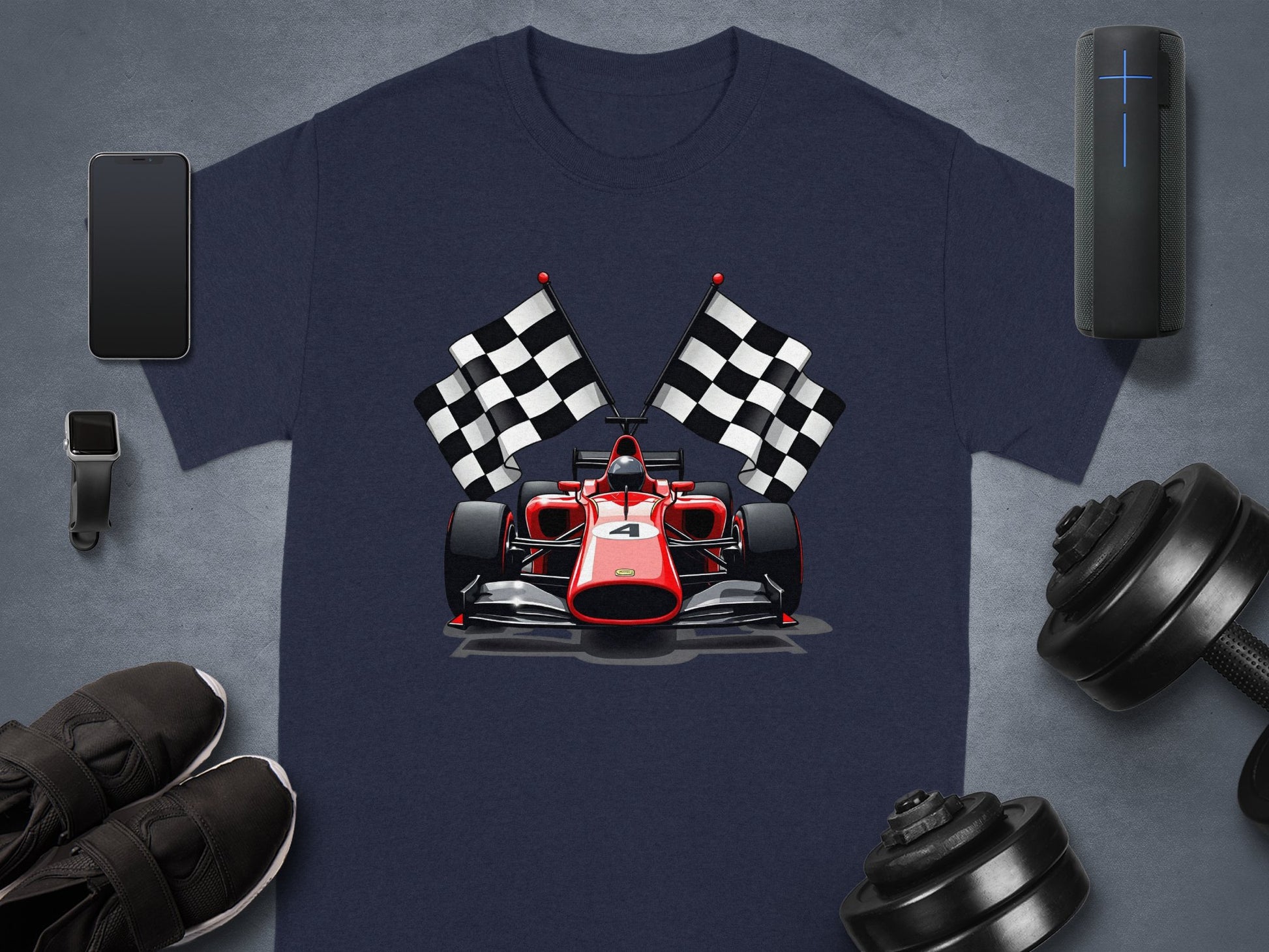 Garment Graphics presents a blue t-shirt showcasing a race car and crossed checkered flags, ideal for motorsport fans. Its set against a gray backdrop with a smartphone, smartwatch, sneakers, wireless speaker, and dumbbell weights.