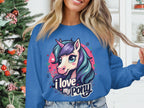 A person wears a vibrant Garment Graphics sweatshirt showcasing a colorful pony-unicorn with the phrase I love my pony. A decorated Christmas tree is partially visible in the background.