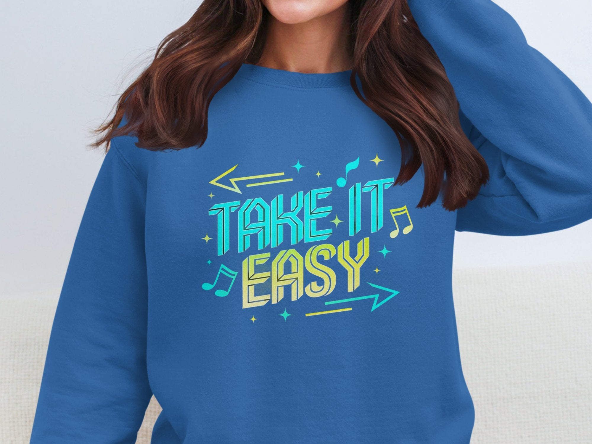 A person wears a Garment Graphics unisex, comfortable sweatshirt featuring the phrase Take it Easy in colorful letters with musical notes and arrows. The persons face is not visible.