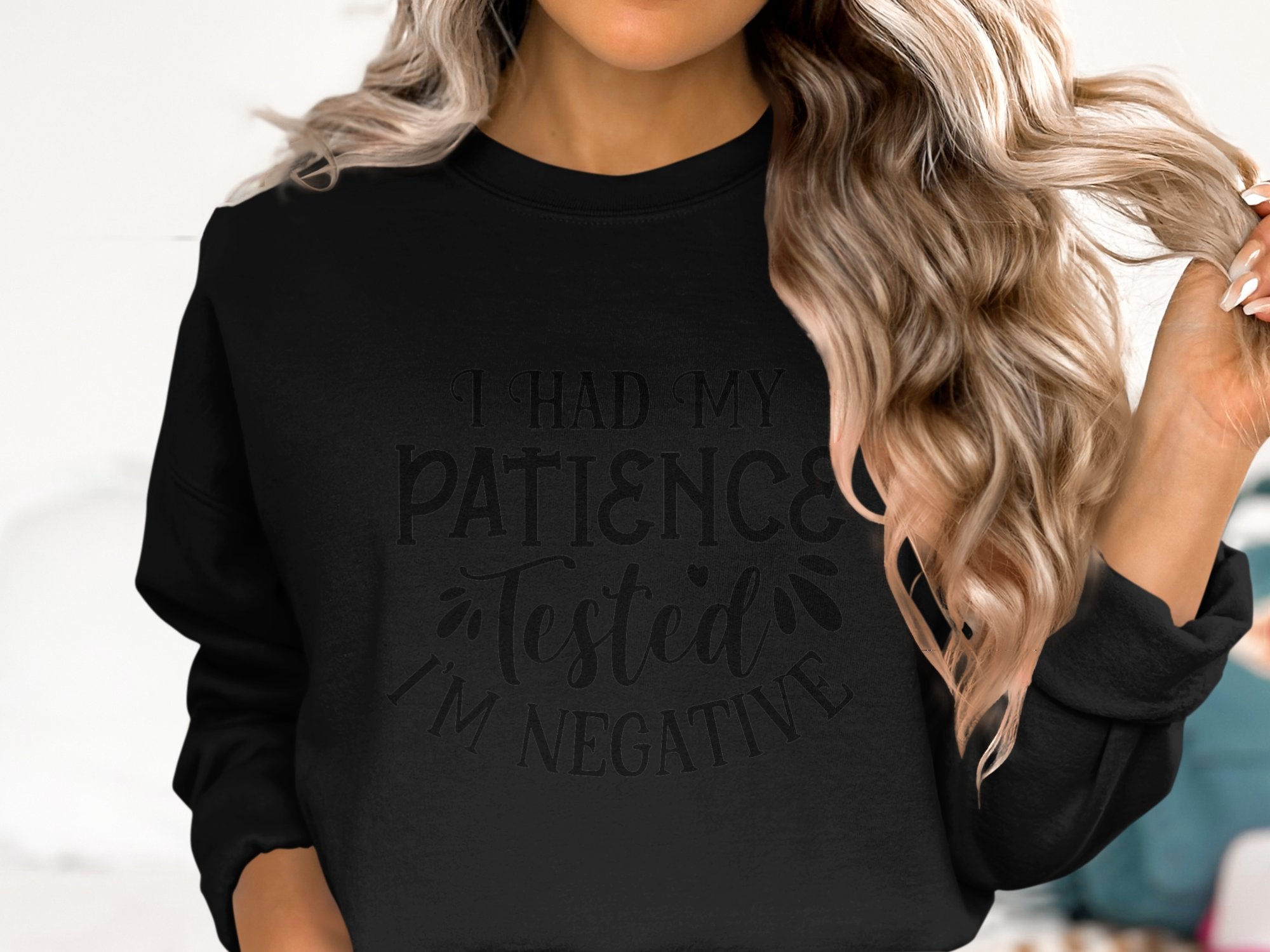 A person with long, wavy blonde hair is wearing a quirky unisex black sweatshirt from Garment Graphics, featuring the text I had my patience tested, Im negative, ideal for casual outings and ensuring a comfortable fit for everyone.