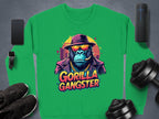 Green Garment Graphics urban sweatshirt with a gorilla graphic sporting sunglasses and a hat, labeled Gorilla Gangster. Nearby are a smartphone, smartwatch, wireless speaker, sneakers, and dumbbells on a dark surface.