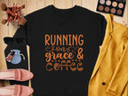A flat lay features a Garment Graphics black graphic sweatshirt reading Running on grace & coffee in unisex sizing, surrounded by pink shoes, yellow jacket, sunglasses, makeup brushes, eyeshadow palette, lipsticks, and a small blue pouch on a wooden surface.