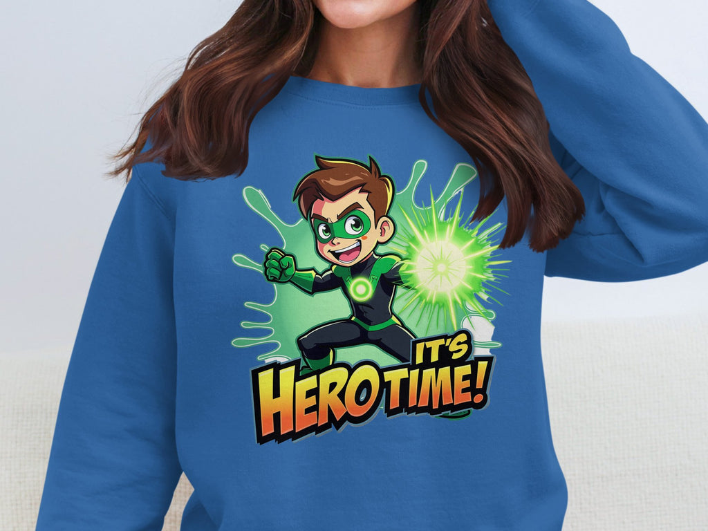 A person wears a blue graphic print sweatshirt by Garment Graphics, featuring a cartoon character with brown hair in a green costume holding a glowing sphere. The text Its Hero Time! appears below. This unisex sweatshirt is perfect for all fans.