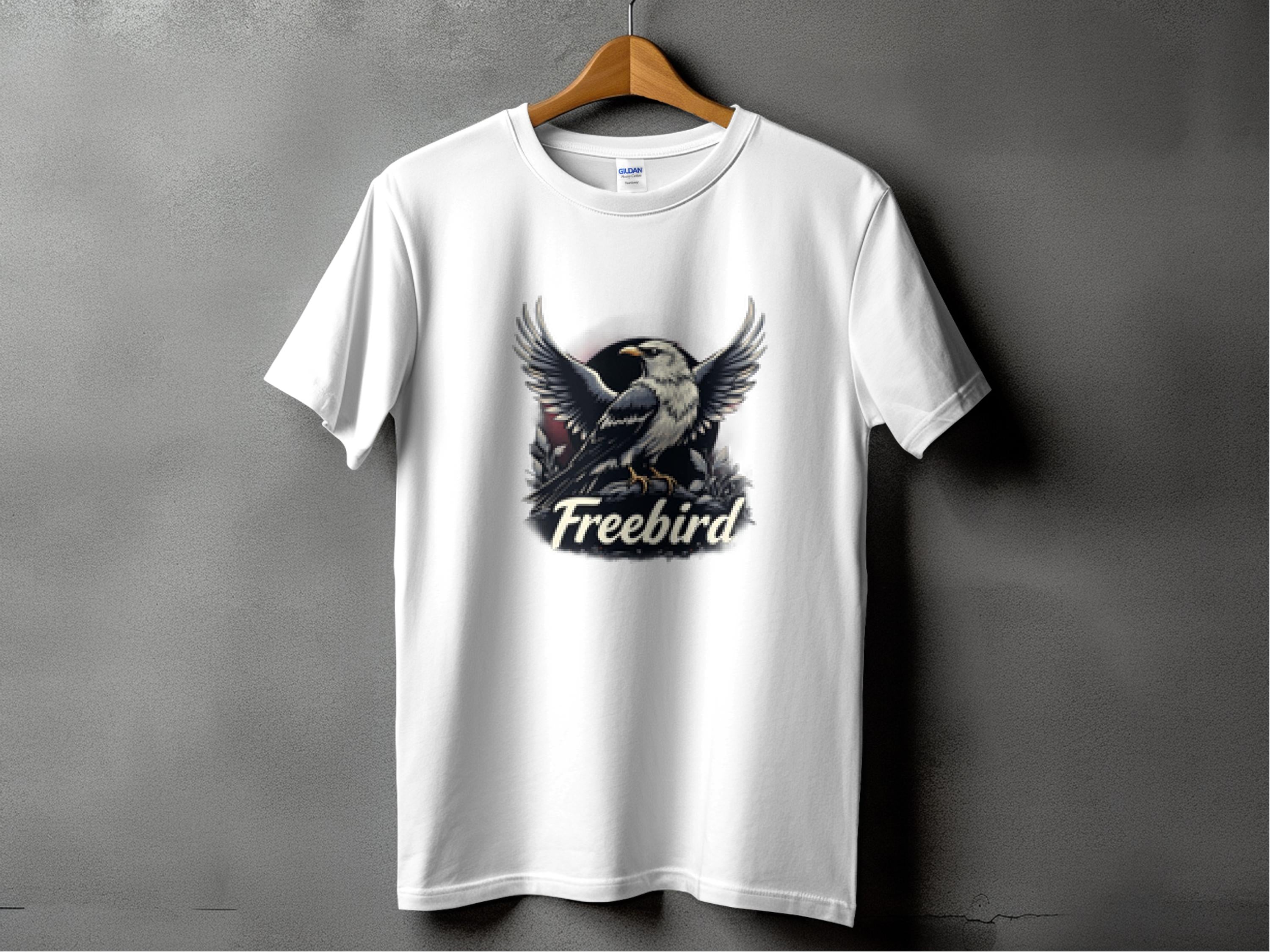 A white Garment Graphics 100% cotton T-shirt hangs against a gray wall, featuring a bold graphic of an eagle with outstretched wings and the text Freebird below.