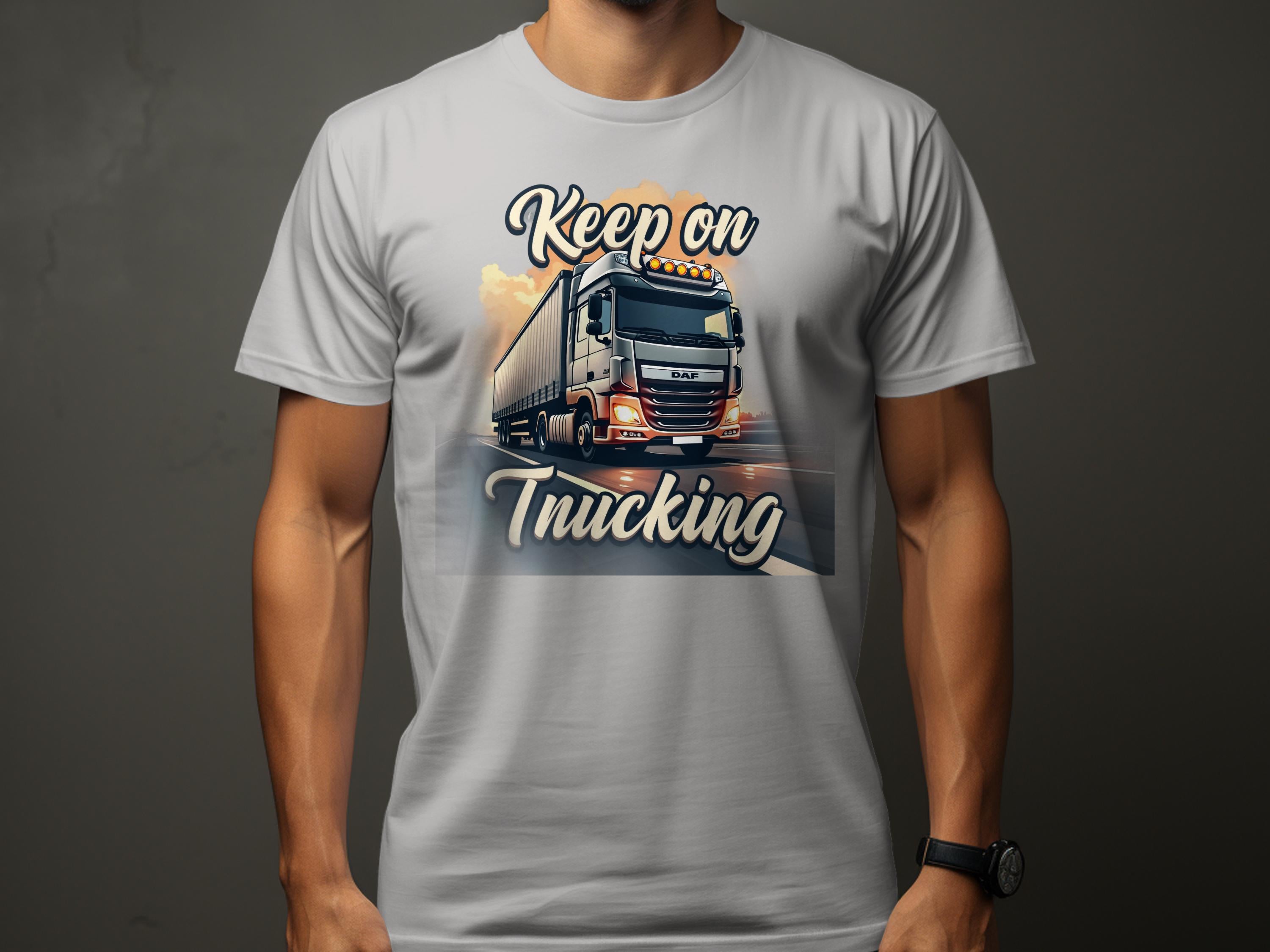 A person wears a Garment Graphics white T-shirt with a graphic print of a large truck on the road. Keep on is printed above and Trucking below. Against a dark background, it highlights their passion for trucks, making it ideal for enthusiasts.