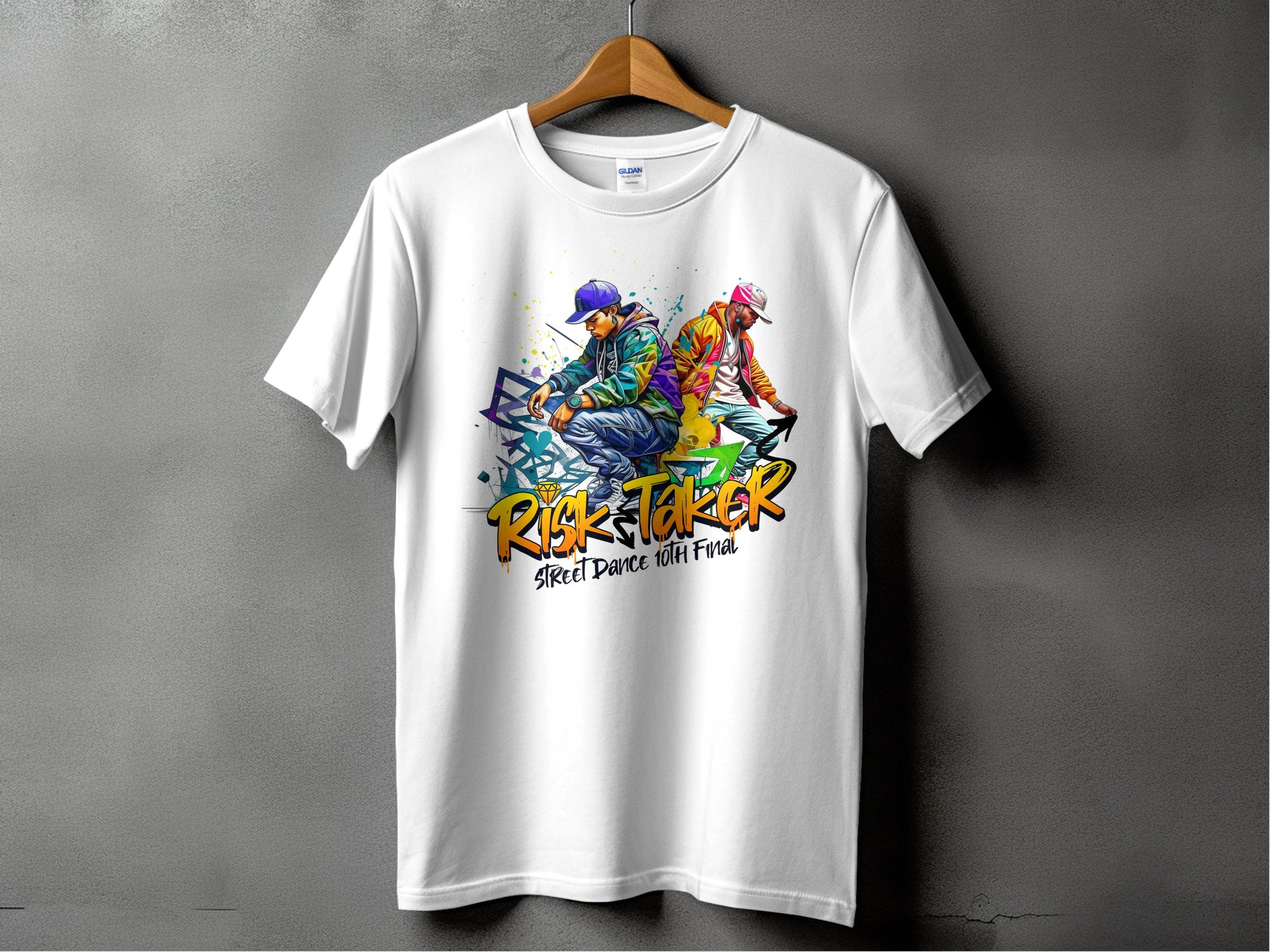 A white t-shirt by Garment Graphics hangs on a plain gray wall, featuring a vibrant graphic of two street dancers in dynamic poses and the words Risk Taker 10th Final T-Shirts, capturing the essence of street dance culture.