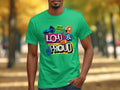 Don a vibrant green Garment Graphics T-shirt, featuring bold Loud & Proud text amidst colorful icons like a megaphone and foam fingers, evoking the spirit of football sports with a backdrop of blurred autumn trees.