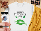 Garment Graphics white sweatshirt features HAPPY ST. PATRICKS DAY text, green lips, and shamrocks, capturing the festive spirit. Surrounded by makeup brushes, eyeshadow palette, sunglasses, lipstick, blue pouch, pink loafers, and a yellow blazer on a wooden surface.