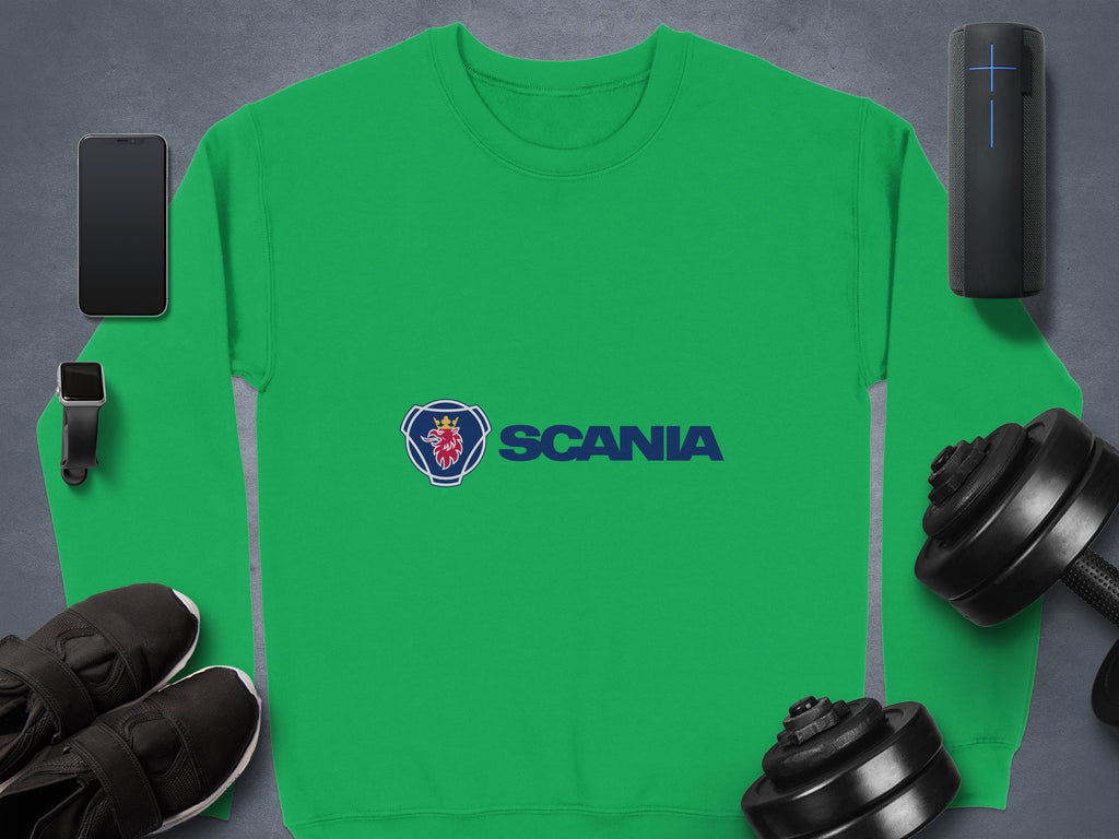 A green Garment Graphics Scania logo sweatshirt for casual outings displays the blue stylized coat of arms and SCANIA, surrounded by a smartphone, smartwatch, speaker, sleek black sneakers, and two dumbbells on a gray surface. Its designed in unisex sizing for ultimate comfort.