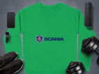 A green Garment Graphics Scania logo sweatshirt for casual outings displays the blue stylized coat of arms and SCANIA, surrounded by a smartphone, smartwatch, speaker, sleek black sneakers, and two dumbbells on a gray surface. Its designed in unisex sizing for ultimate comfort.