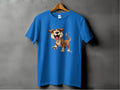 Garment Graphics presents a blue T-shirt, ideal for dog enthusiasts, displayed on a wooden hanger against a gray backdrop. It showcases a cheerful cartoon dog with fluffy fur and big eyes, making it perfect for anyone who loves their furry friends.