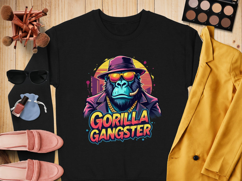 This urban black sweatshirt by Garment Graphics features a Gorilla Gangster in a hat and sunglasses, smoking a cigar, with makeup items, chic sunglasses, pink shoes, and a yellow blazer on a wooden surface. Perfect for adding edgy style to your wardrobe.