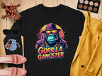 This urban black sweatshirt by Garment Graphics features a Gorilla Gangster in a hat and sunglasses, smoking a cigar, with makeup items, chic sunglasses, pink shoes, and a yellow blazer on a wooden surface. Perfect for adding edgy style to your wardrobe.