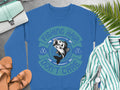 Garment Graphics offers a blue fishing sweatshirt with a fish graphic and Fishing Hair Dont Care in green and blue. The ensemble is styled with sandals, a green striped shirt, watch, handbag, and ferns on gray, perfect for fishing enthusiasts.