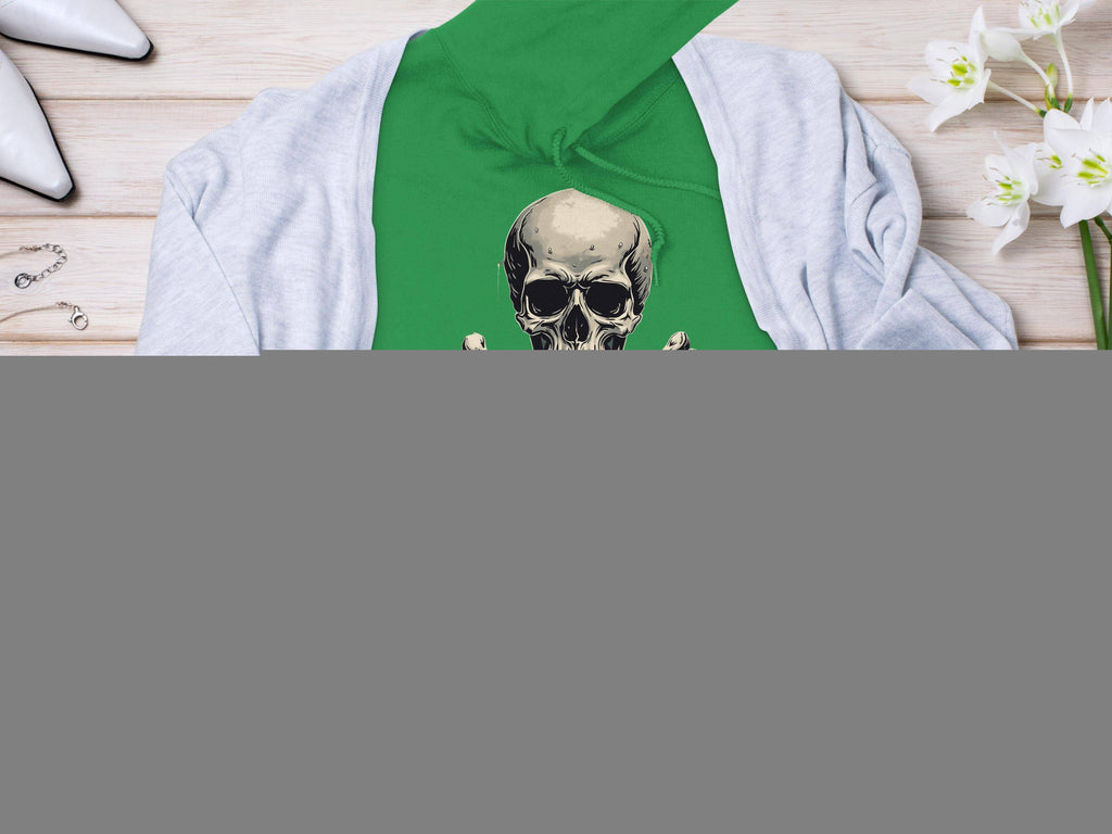A vibrant green Garment Graphics hoodie with a skull and crossbones design rests on a light wooden surface. Its accented by a light gray cardigan, chic white heels, elegant jewelry, and a vase of stunning white flowers.