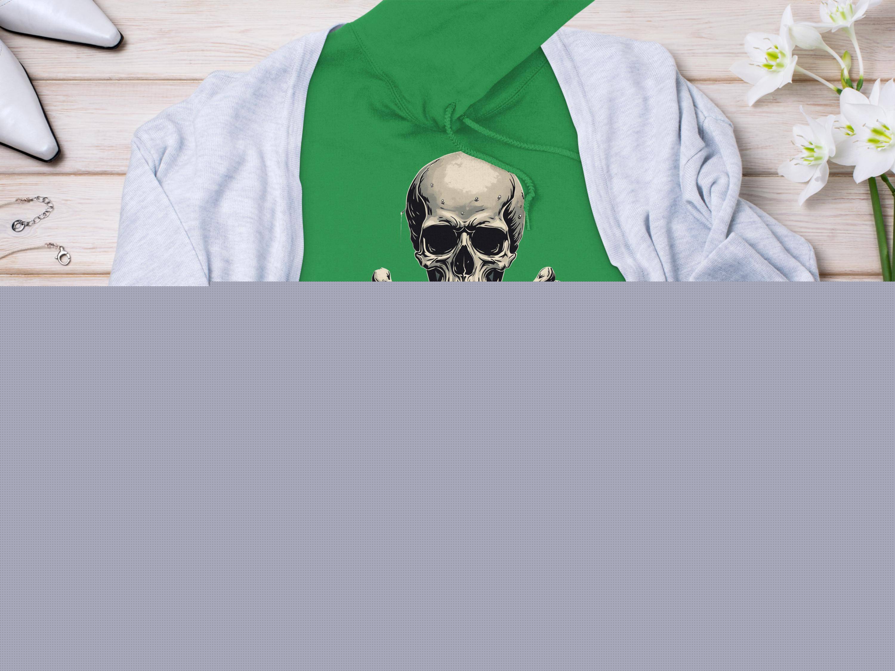 A vibrant green Garment Graphics hoodie with a skull and crossbones design rests on a light wooden surface. Its accented by a light gray cardigan, chic white heels, elegant jewelry, and a vase of stunning white flowers.
