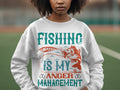 A person wears a Garment Graphics white sweatshirt featuring the slogan Fishing Is My Anger Management in bright turquoise and orange lettering, accompanied by a fish and lure design. The pleasantly blurry outdoor background makes it ideal for fishing enthusiasts.