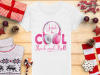 The Garment Graphics white headphones t-shirt displays a pink headphones design with Just be cool, Rock and Roll text. Its ideal for music lovers, shown among wrapped gifts, pine cones, red stars, a candy cane, a red-and-white sweater, and red-berried sprigs on wood.