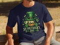 A person sits on a wooden bench wearing a navy Garment Graphics T-shirt that exudes Irish pride, featuring a leprechaun in a green top hat, surrounded by shamrocks with St Patricks Day printed boldly in white.