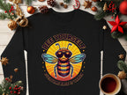 Flat lay of a Garment Graphics black shirt displaying a bee with sunglasses and the text Bee Yourself above and Everyone Else Is Taken below in retro font. Ideal for unisex sizing, its surrounded by holiday decorations and a coffee cup on a wooden surface.