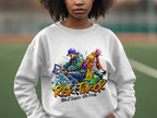 A person in a white sweatshirt displays a vibrant Garment Graphics design featuring two dancers and Risk Taker Street Dance 10th Final. The blurred sports field backdrop encapsulates the street dance finals energy.