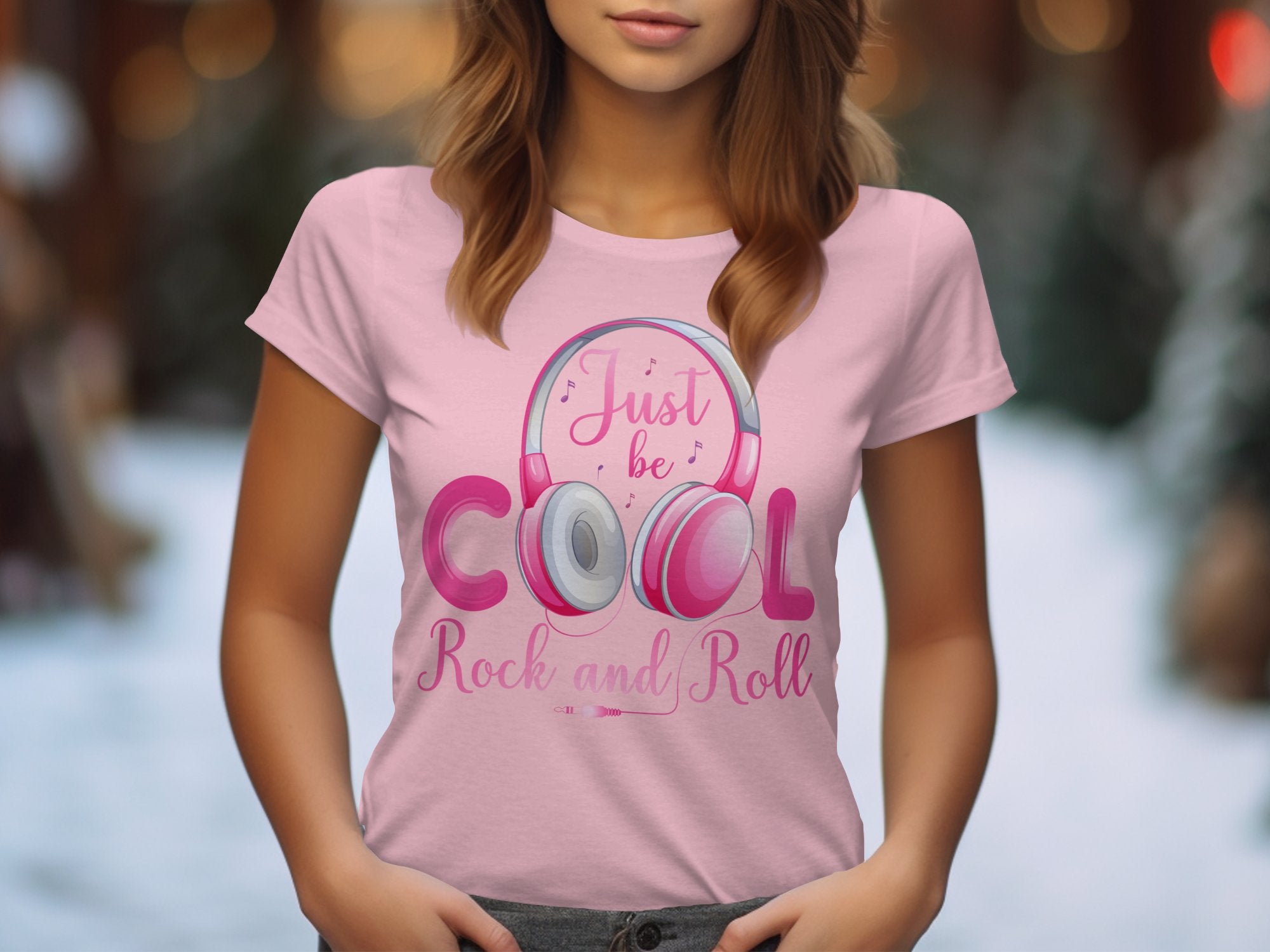 A woman wears a Garment Graphics pink t-shirt with Just be Cool, Rock and Roll and a headphone illustration. Ideal for music lovers, the soft blend of warm and cool tones captures the essence of the headphones t-shirt trend.