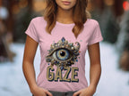 A person in a pink Garment Graphics T-shirt featuring a large eye graphic with artistic accents and GAZE elegantly printed below. This womens Gaze graphic T-shirt sits against a softly blurred background.