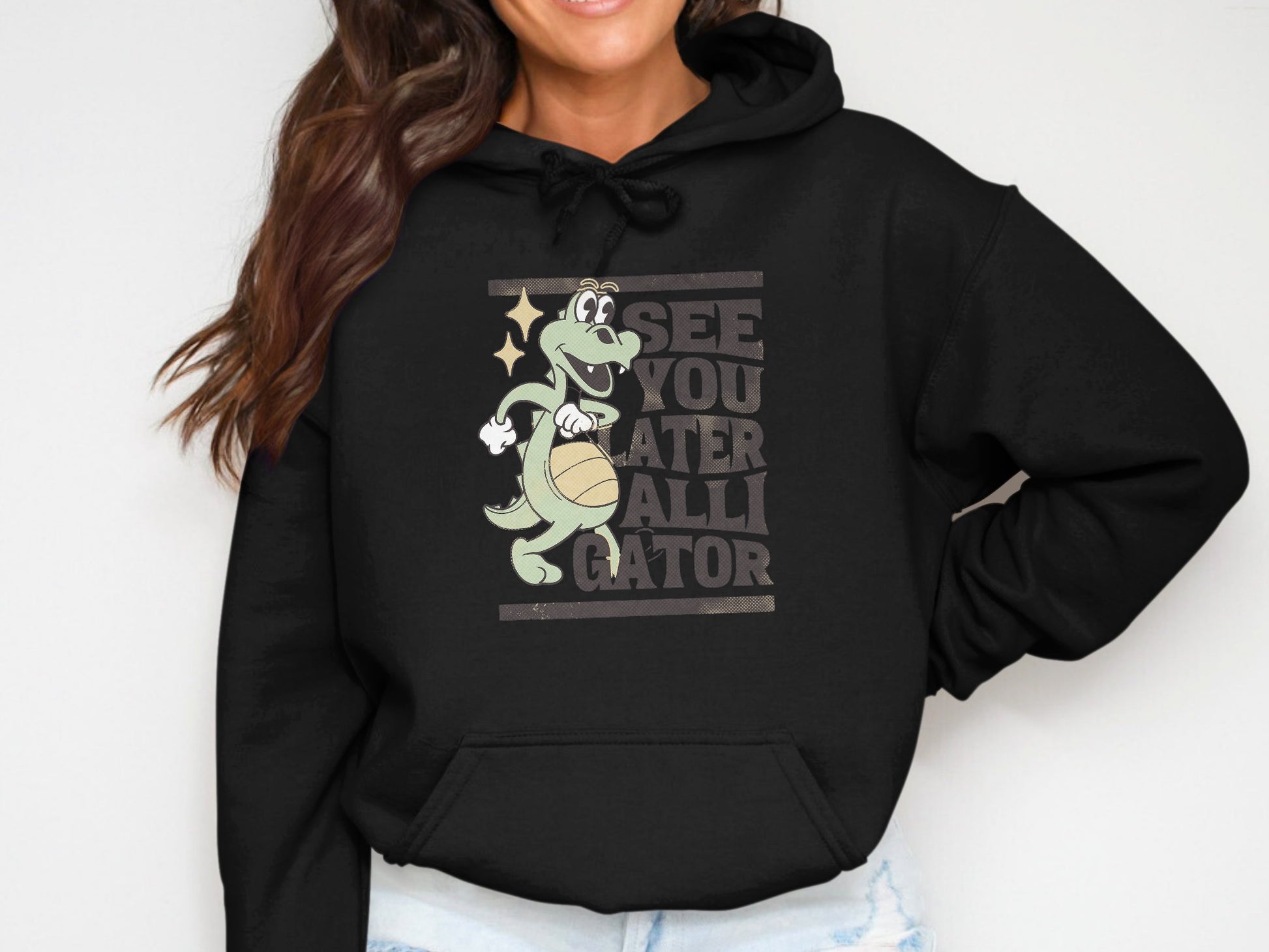 A person showcases a classic fit hoodie from Garment Graphics, displaying a playful See You Later Alligator design with a gator holding a basketball. Theyre smiling widely, and the torso view emphasizes the charming graphic.