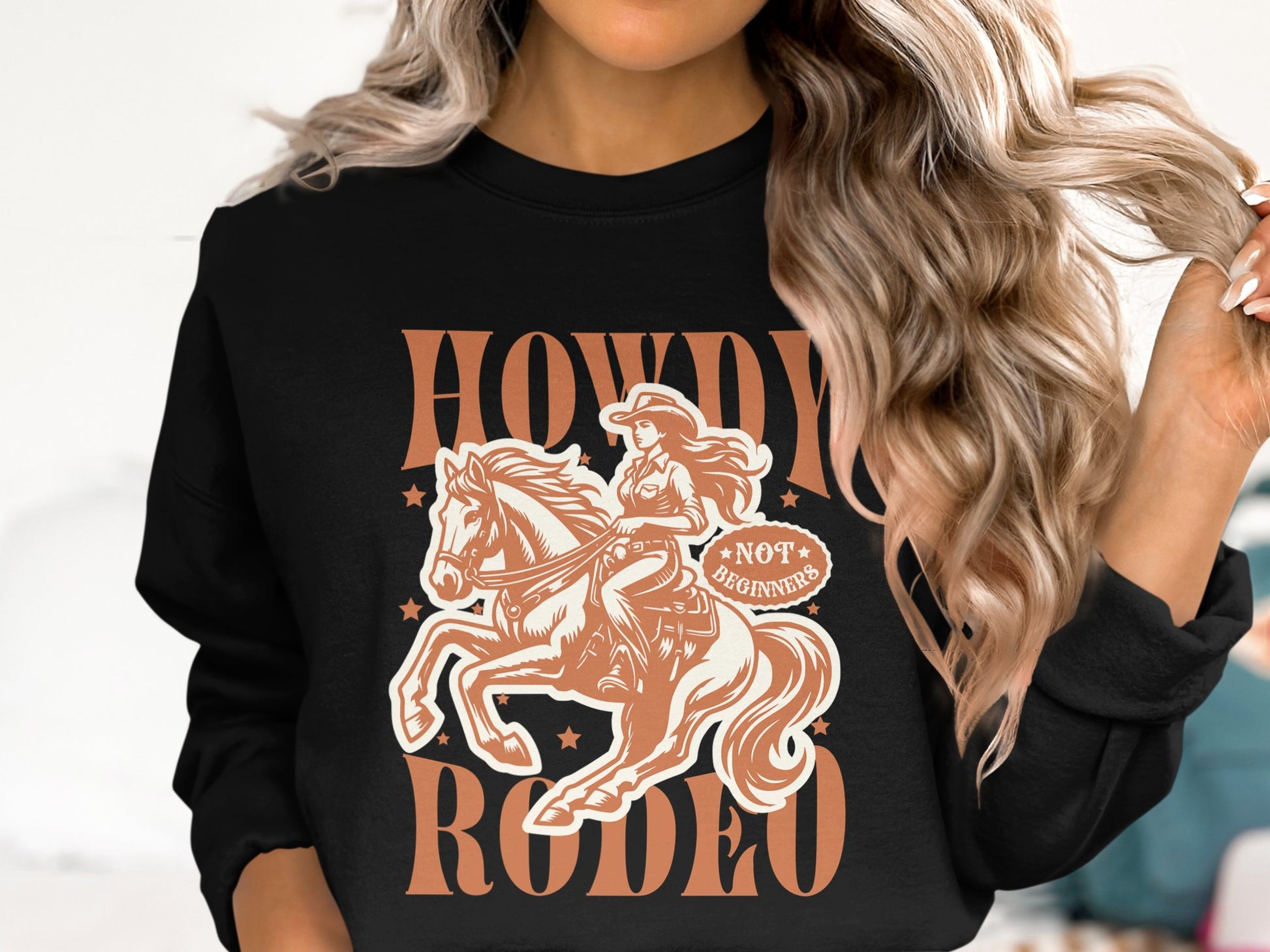 A person with long wavy hair wears a Garment Graphics Howdy Rodeo sweatshirt, featuring a cowgirl and stars. The text declares Not a Beginner. Ideal for rodeo fans, it captures the cowboy spirit while keeping their identity concealed.