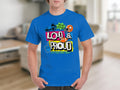 A person in a blue Garment Graphics T-shirt featuring colorful text and graphics, including Loud & Proud, a megaphone, star, and foam finger symbols. Its ideal for expressing passion for football sports, with a blurred interior setting in the background.