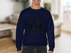 A person wears a dark blue ENJOY Classic Car sweatshirt by Garment Graphics, featuring a vintage automobile image. The softly blurred backdrop reveals a living room with beige furniture.