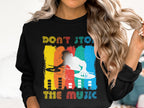 A person models a Garment Graphics black sweatshirt featuring a vibrant DJ design with a silhouette and DONT STOP THE MUSIC text. The background bursts with blue, orange, yellow, and red vertical stripes—ideal for music lovers.