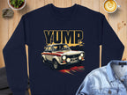 A navy sweatshirt by Garment Graphics showcases a bold YUMP design with a vintage rally car illustration. The scene includes a wooden table, a latte in the top right corner, and a light denim shirt partially visible at the bottom right.