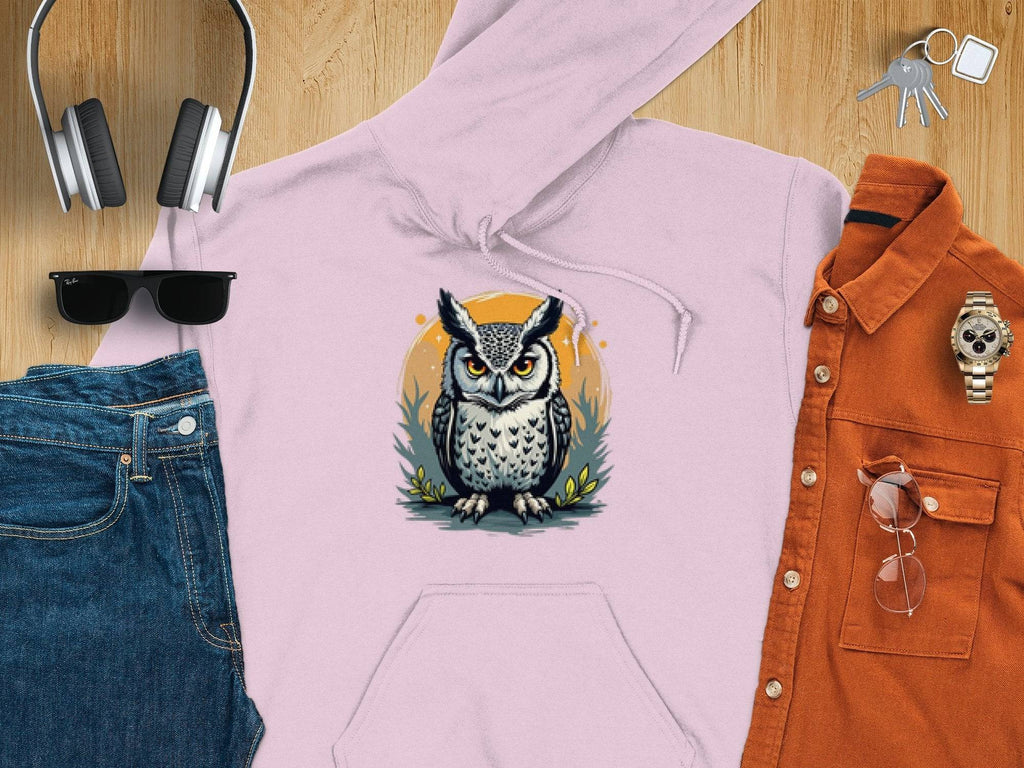 A Garment Graphics light pink owl artwork hoodie lies on a wooden surface, surrounded by jeans, an orange button-up shirt, headphones, sunglasses, a watch, and keys.