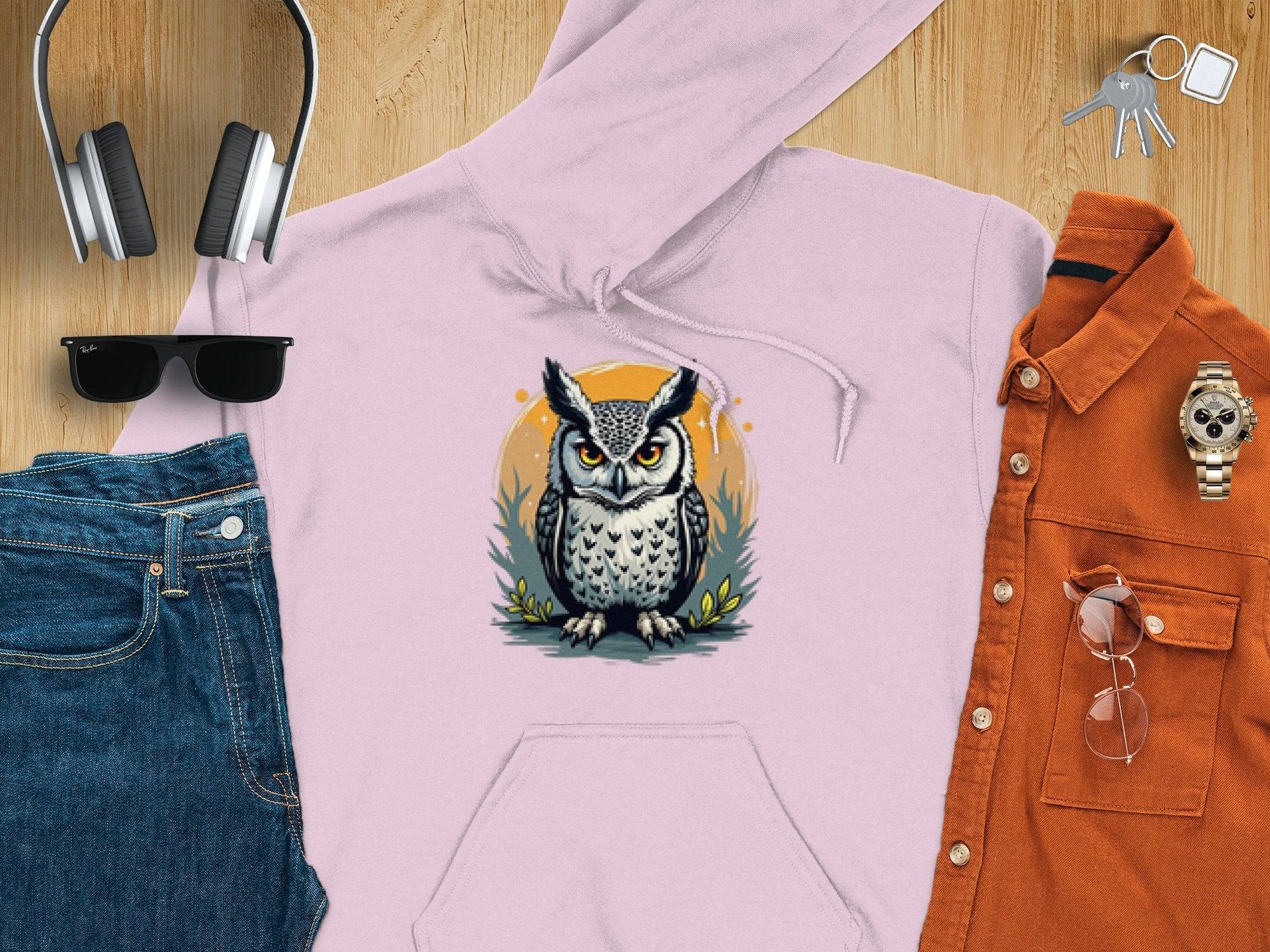 A Garment Graphics light pink owl artwork hoodie lies on a wooden surface, surrounded by jeans, an orange button-up shirt, headphones, sunglasses, a watch, and keys.
