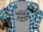 A Garment Graphics gray t-shirt saying I had my patience tested, Im negative lies on wood. Ideal for casual outings, its paired with an open blue and green plaid shirt. Black headphones, a camera, and a disposable coffee cup complete the look.